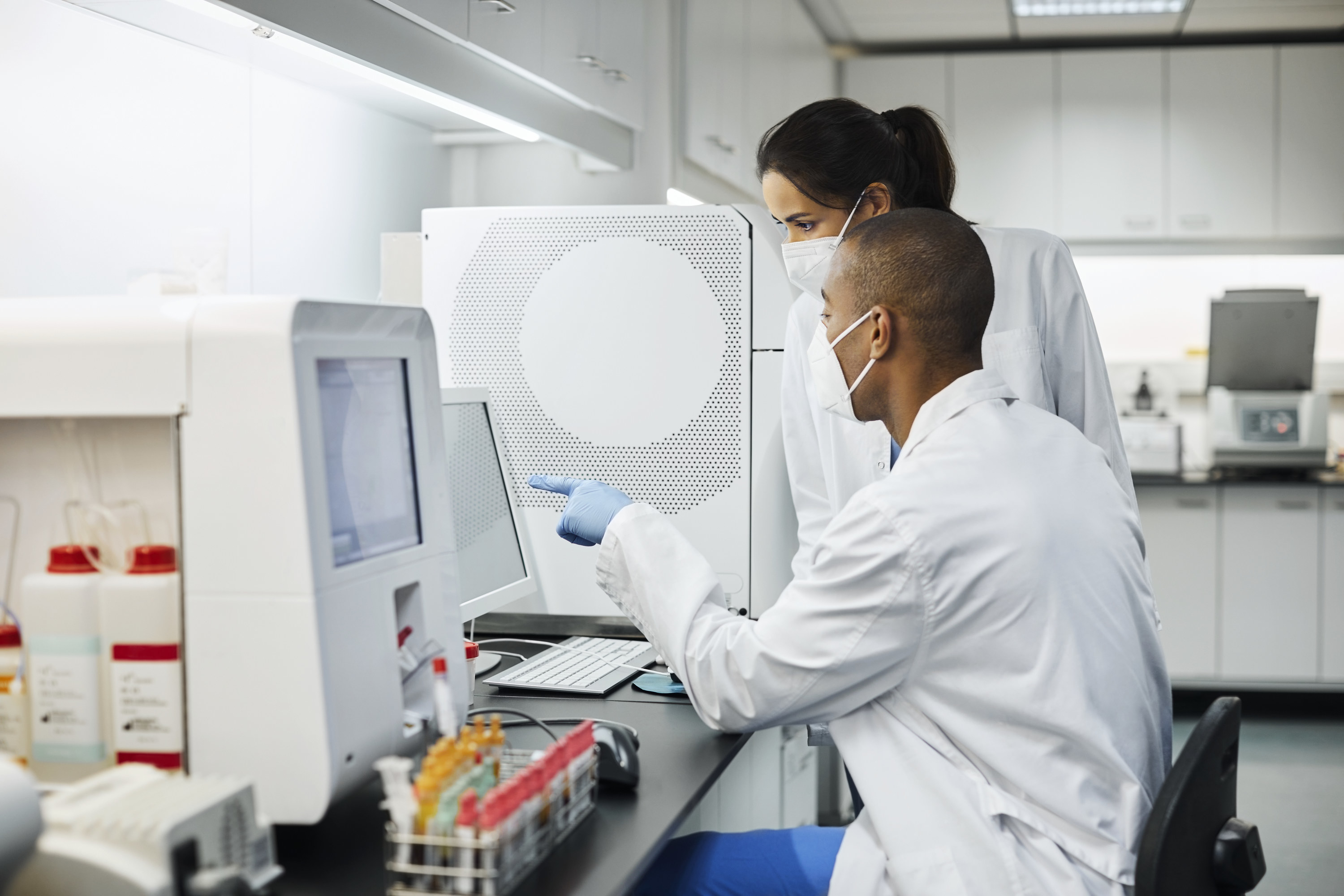 A man and woman in white lab coats looking at a computer screen together