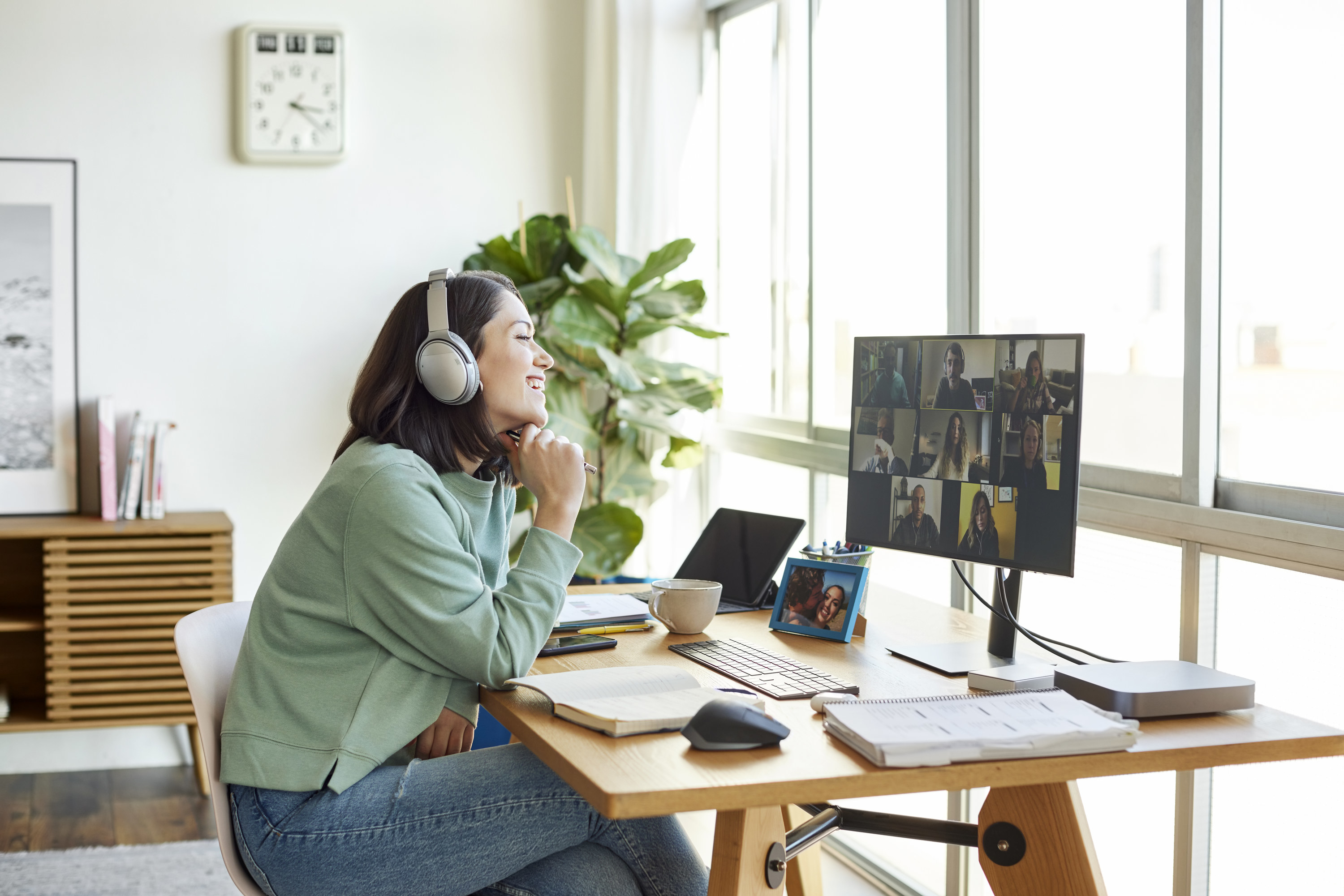 A woman with headphones on sitting at a desk in a virtual meeting with other people