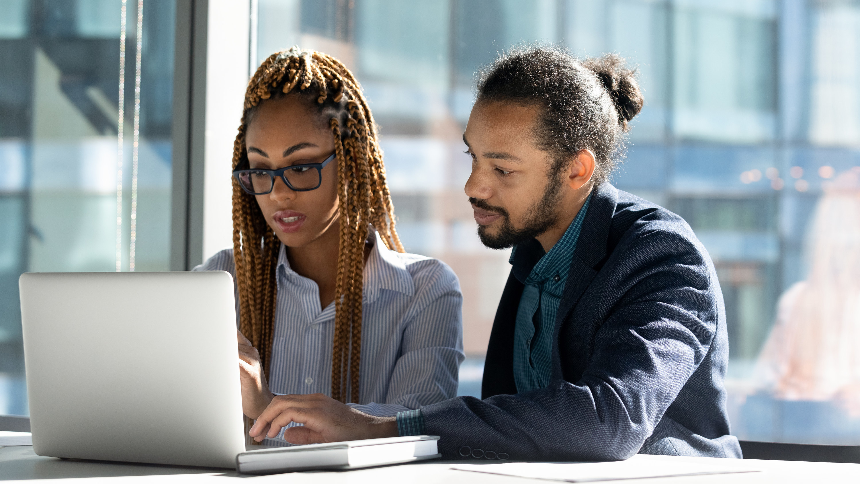 A man and a woman looking at the screen of a laptop sitting next to each other