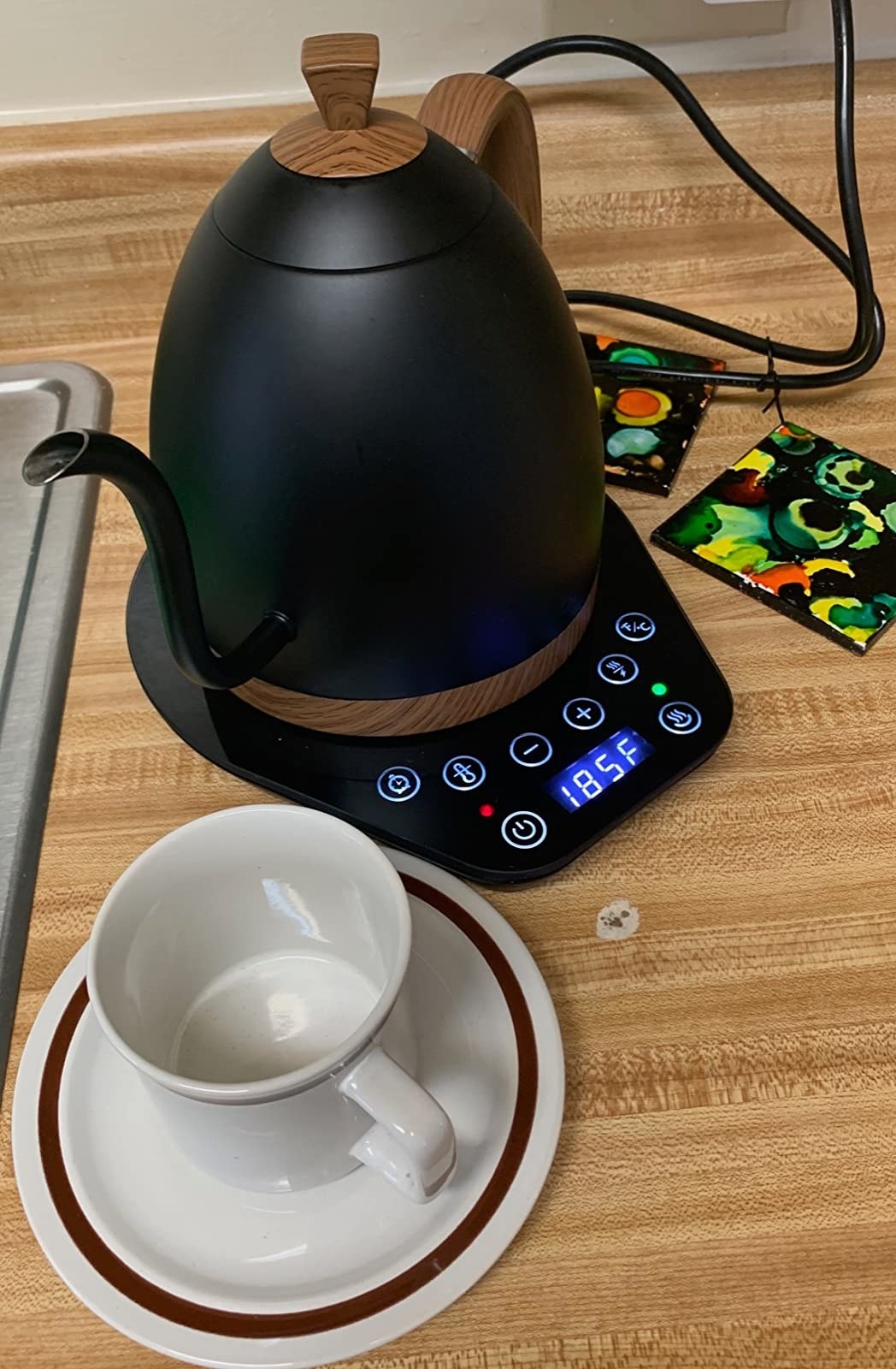Black matte electric tea kettle on top of black panel with digital display of functions and temperature
