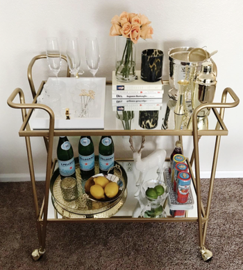 reviewer's full bar cart with bottles of drinks and cans on the bottom
