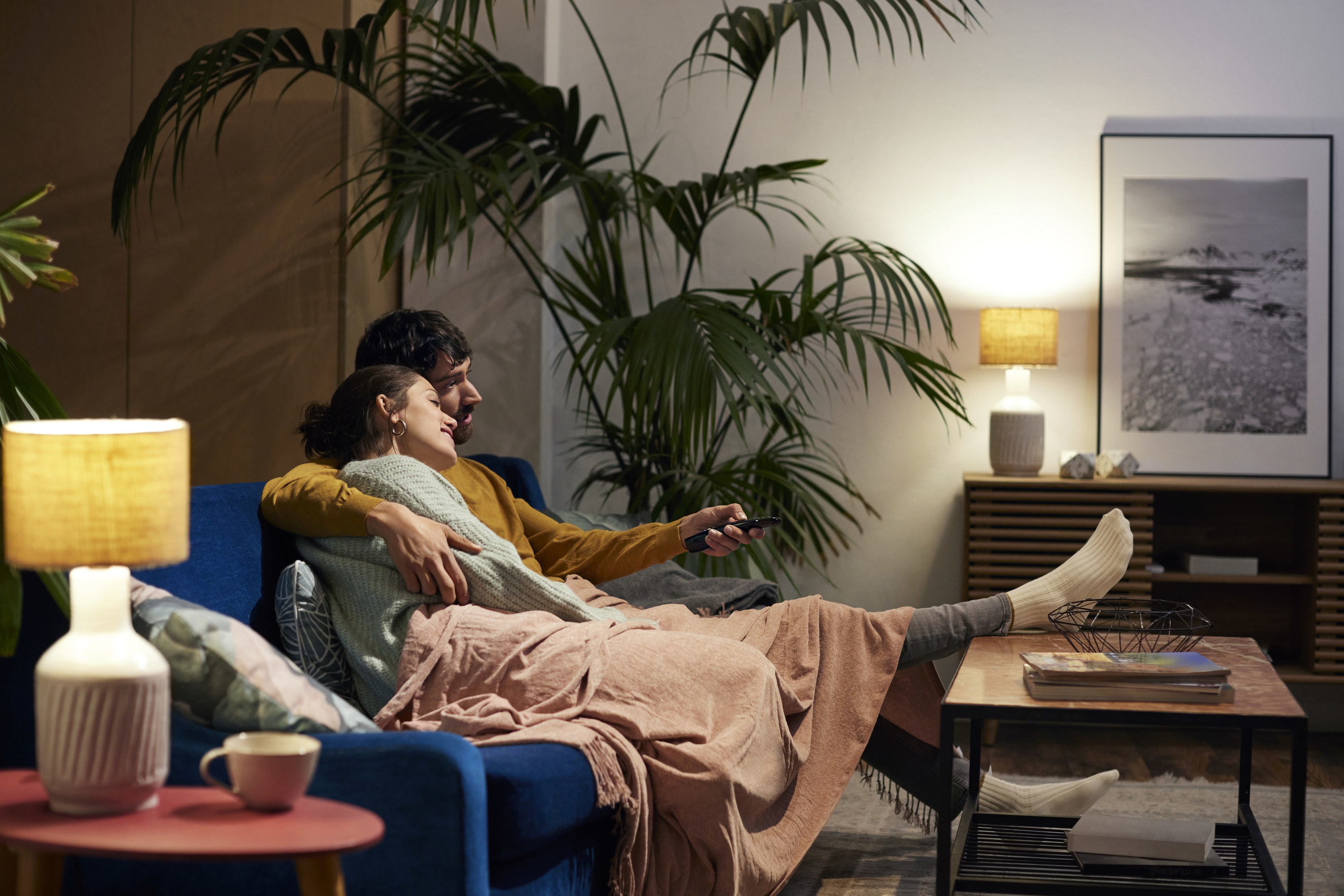 A man and woman hugging on a couch under a blanket together