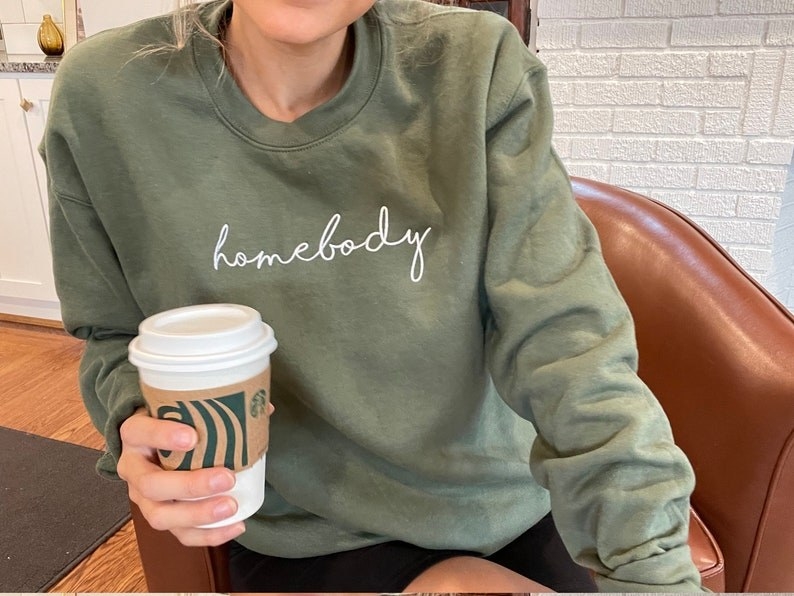 a model wears the green sweatshirt that reads &quot;homebody&quot; in white cursive