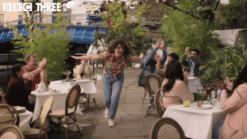 A gif of Jessie running through an outdoor restaurant patio with her arms outstretched laughing in Starstruck