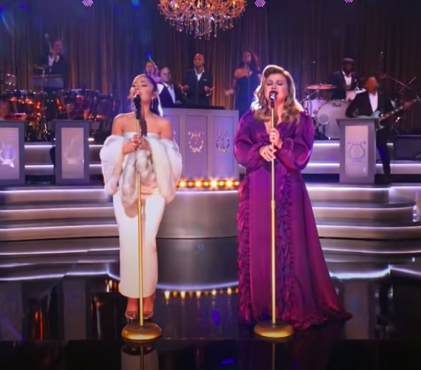 Ari is wearing a simple strapless ankle-length dress with a faux fur stole and Kelly is wearing a long-sleeved floor-length gown with ruffle details down the front
