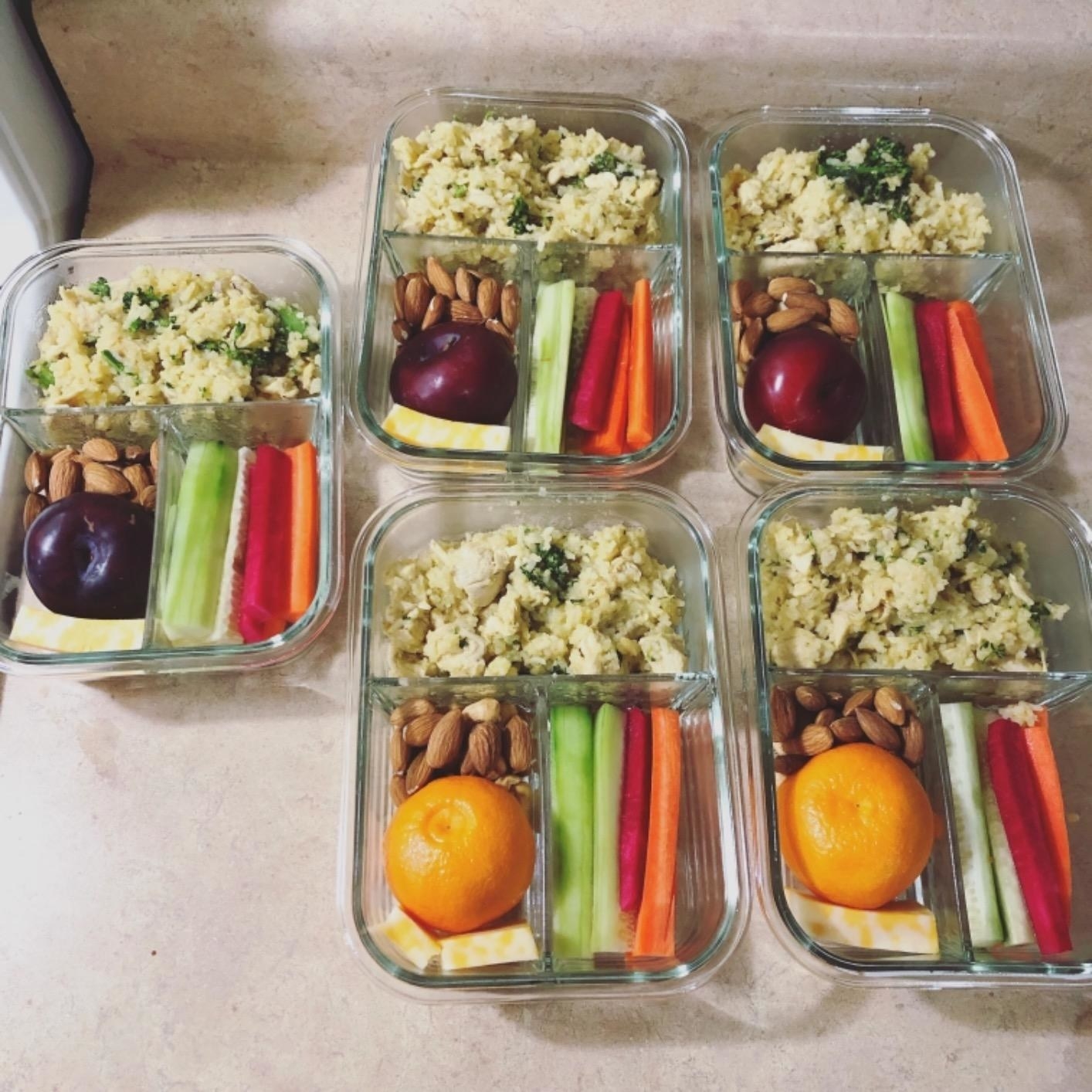 a reviewer shows five containers filled with  veggies, fruit, and chicken salad in each section.