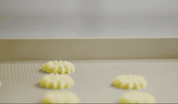 GIF showing someone using the cookie press to stamp out flower-shaped cookie dough on a sheet tray
