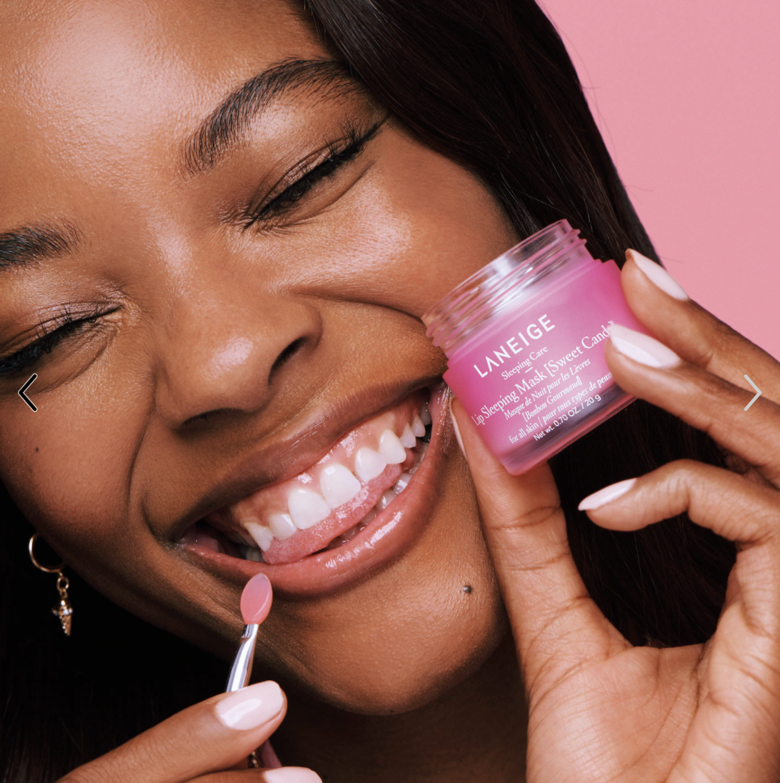 model holding the jar of product and smiling applying the lip mask to her lips with an applicator
