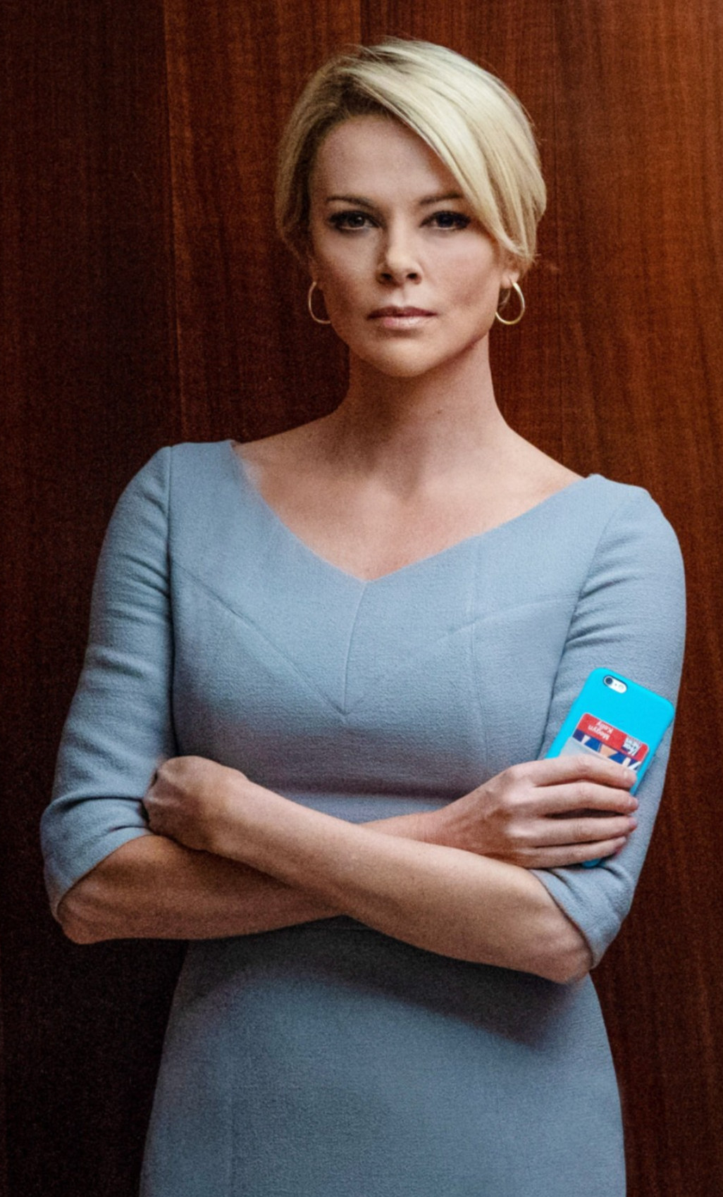 Theron folding her arms while wearing a tight dress and short, blonde hair in an elevator