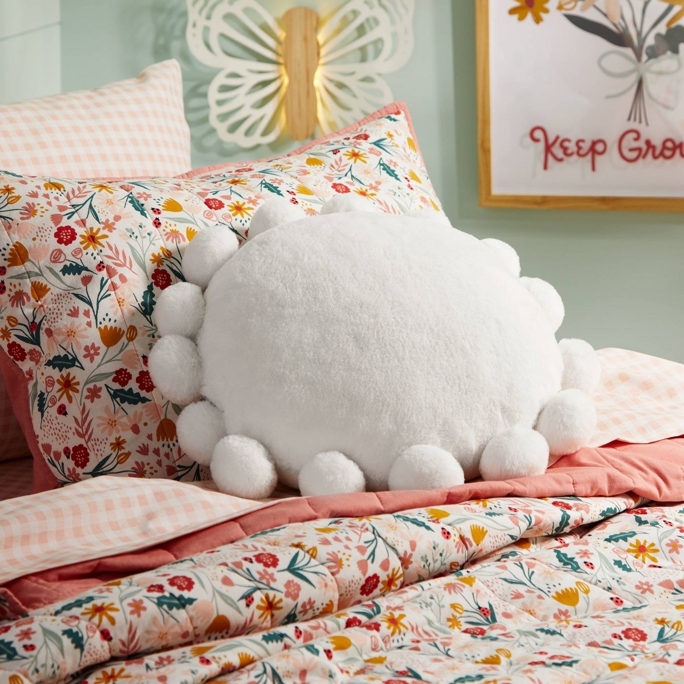 A white pom pom pillow on a pink floral bed