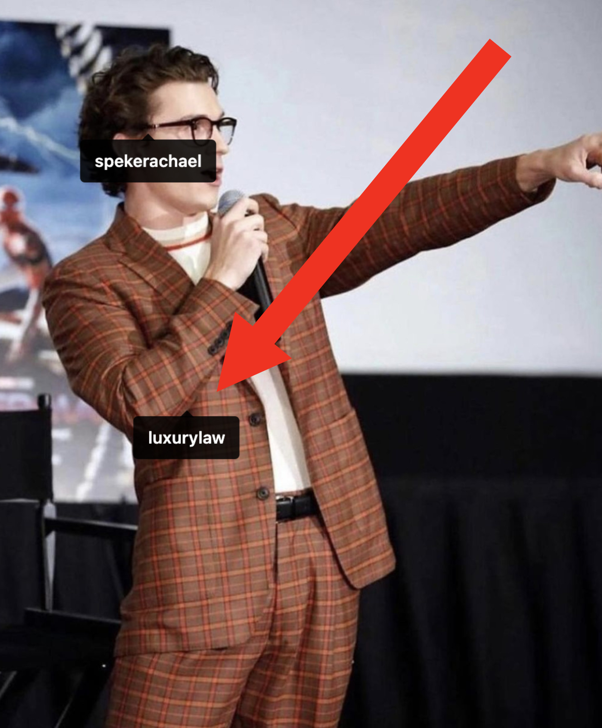 Tom onstage at a Spider-Man event in a plaid suit with a lightly colored shirt with Law tagged on the outfit