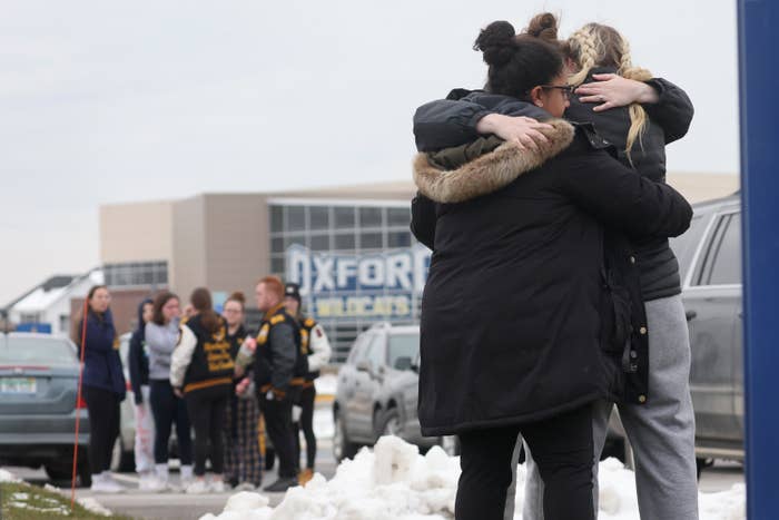 People embrace in a snowy parking lot outside Oxford High School