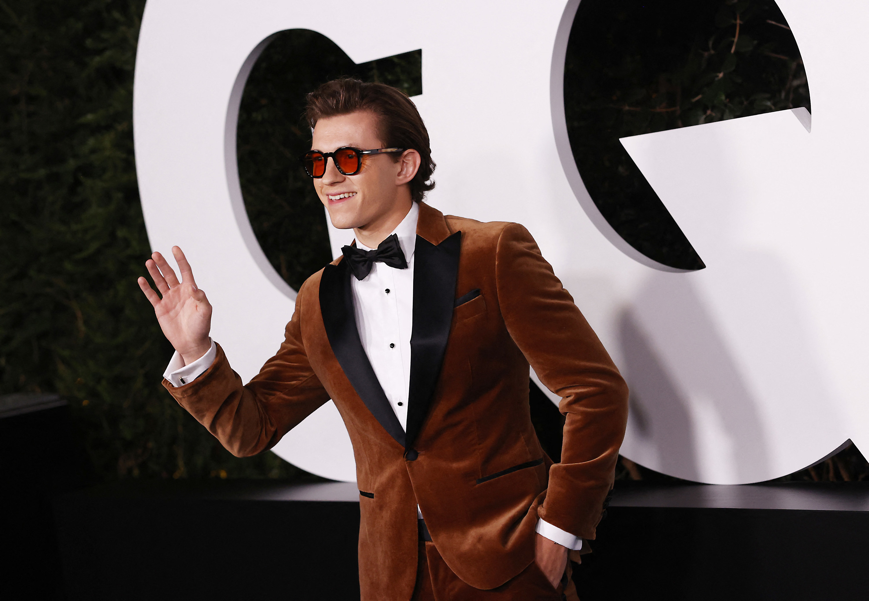 Tom waves at the GQ awards while wearing a dapper velvet tux and tinted sunglasses
