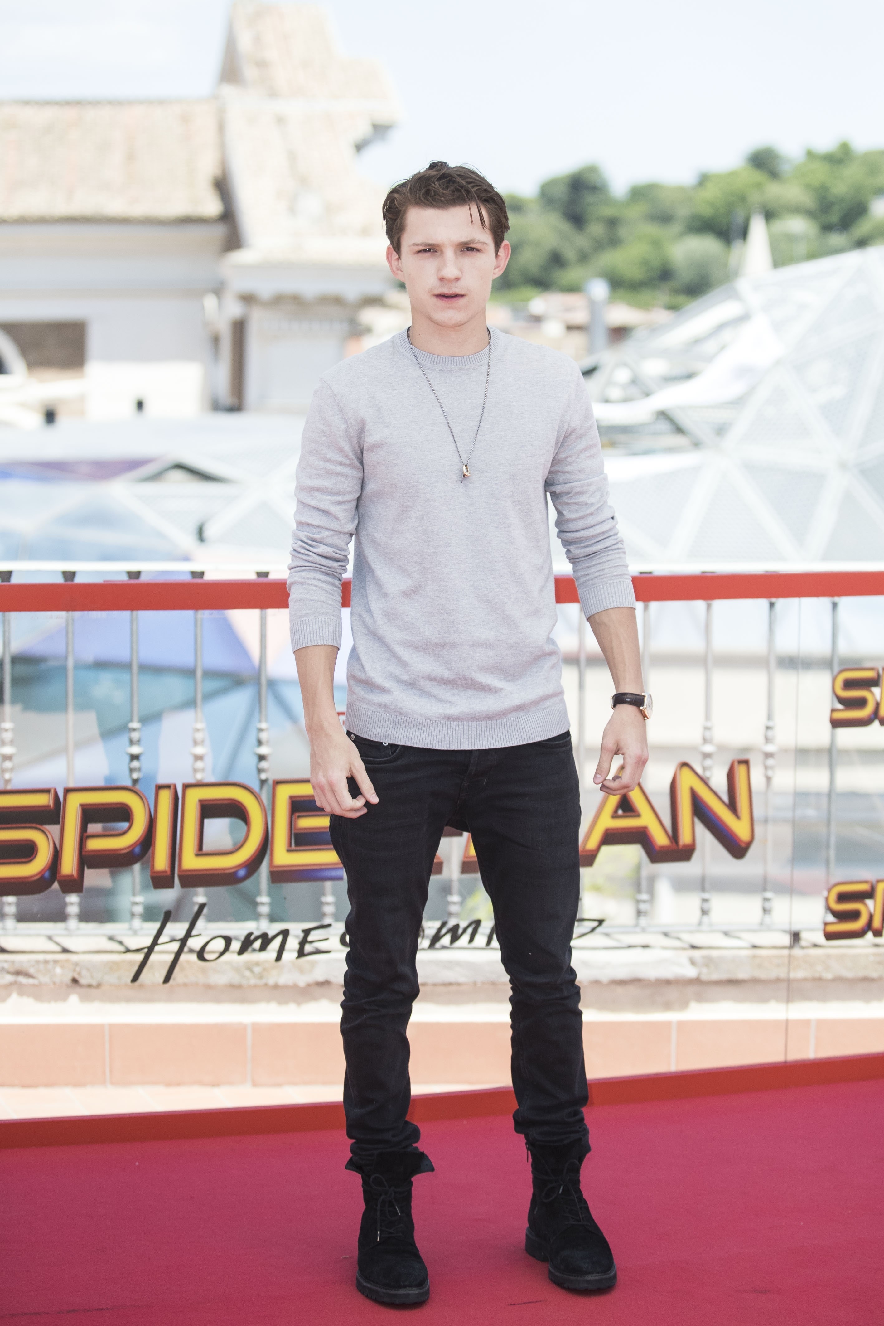 Tom at a red carpet event in a long-sleeved sweater shirt, denim pants, and boots
