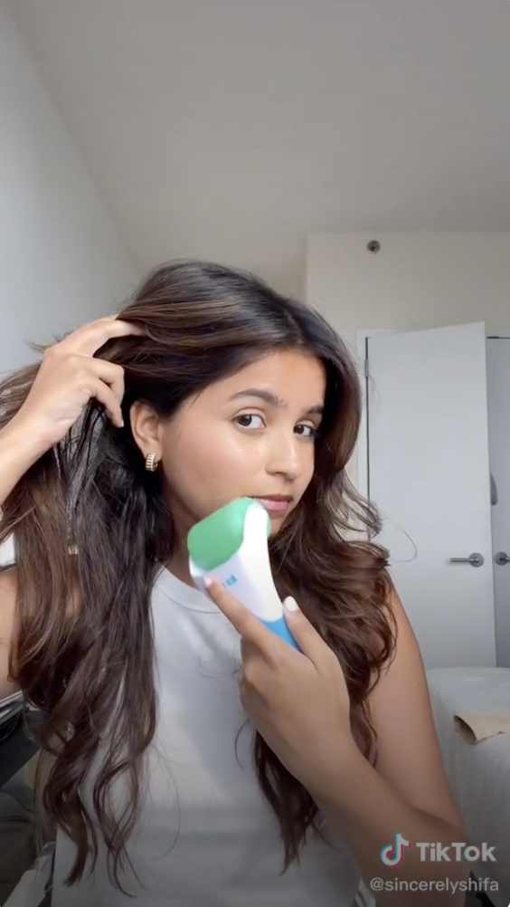 A girl using a ice roller to her face and holding back her hair