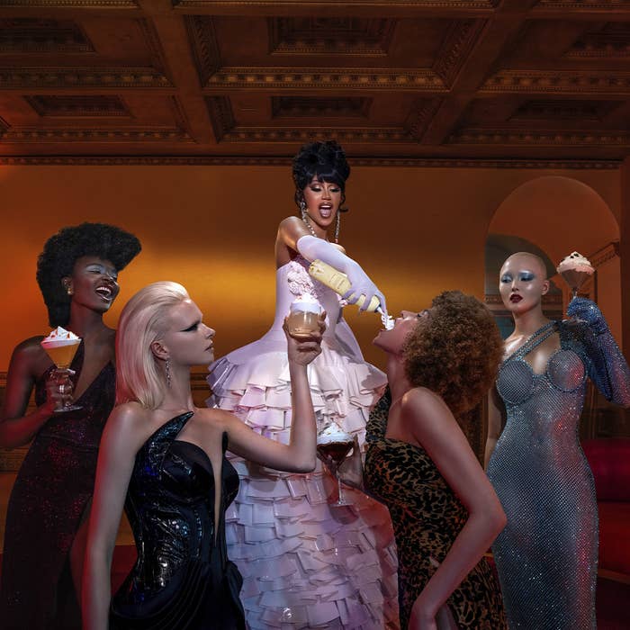Promo image of Cardi B in a luxurious gown spraying her boozy whipped cream into the mouths of four models, holding whipped cream-topped cocktails