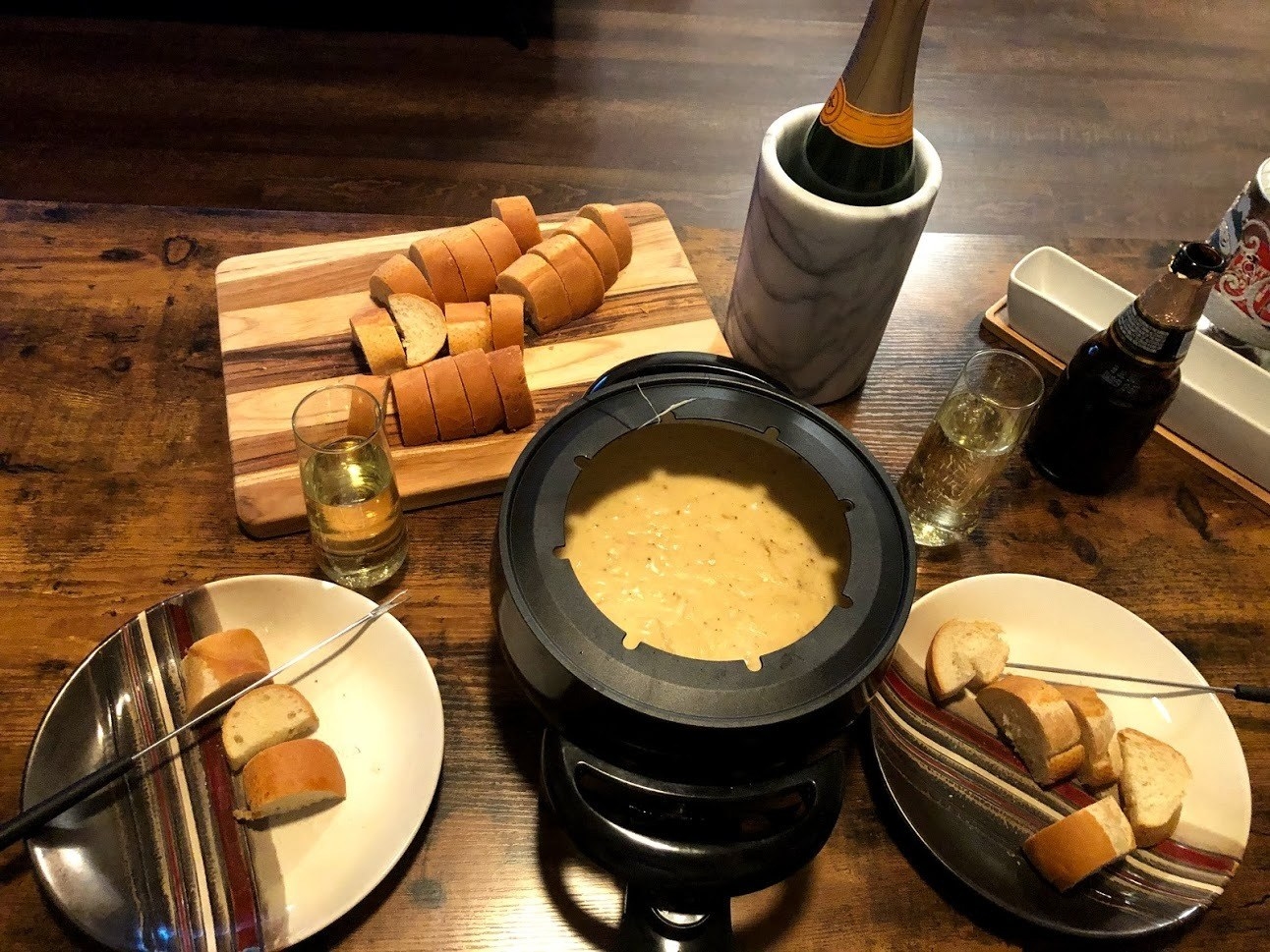 A reviewer&#x27;s black fondue maker filled with cheese, with bread and wine on the sides