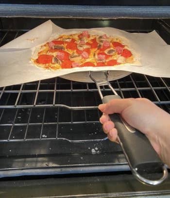 A reviewer photo of them putting a pizza in their oven
