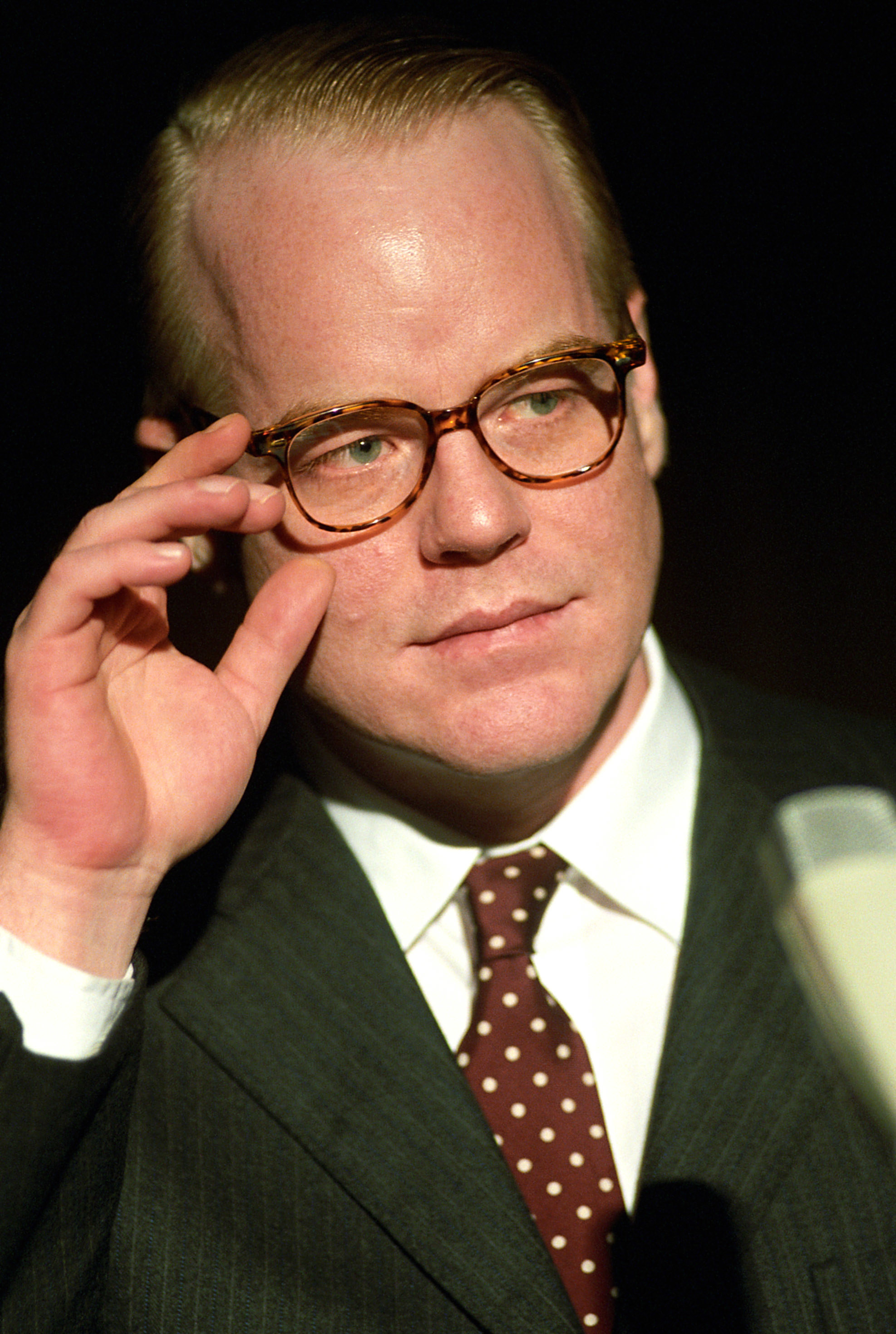 Hoffman wearing round glasses, suit and tie like Truman Capote