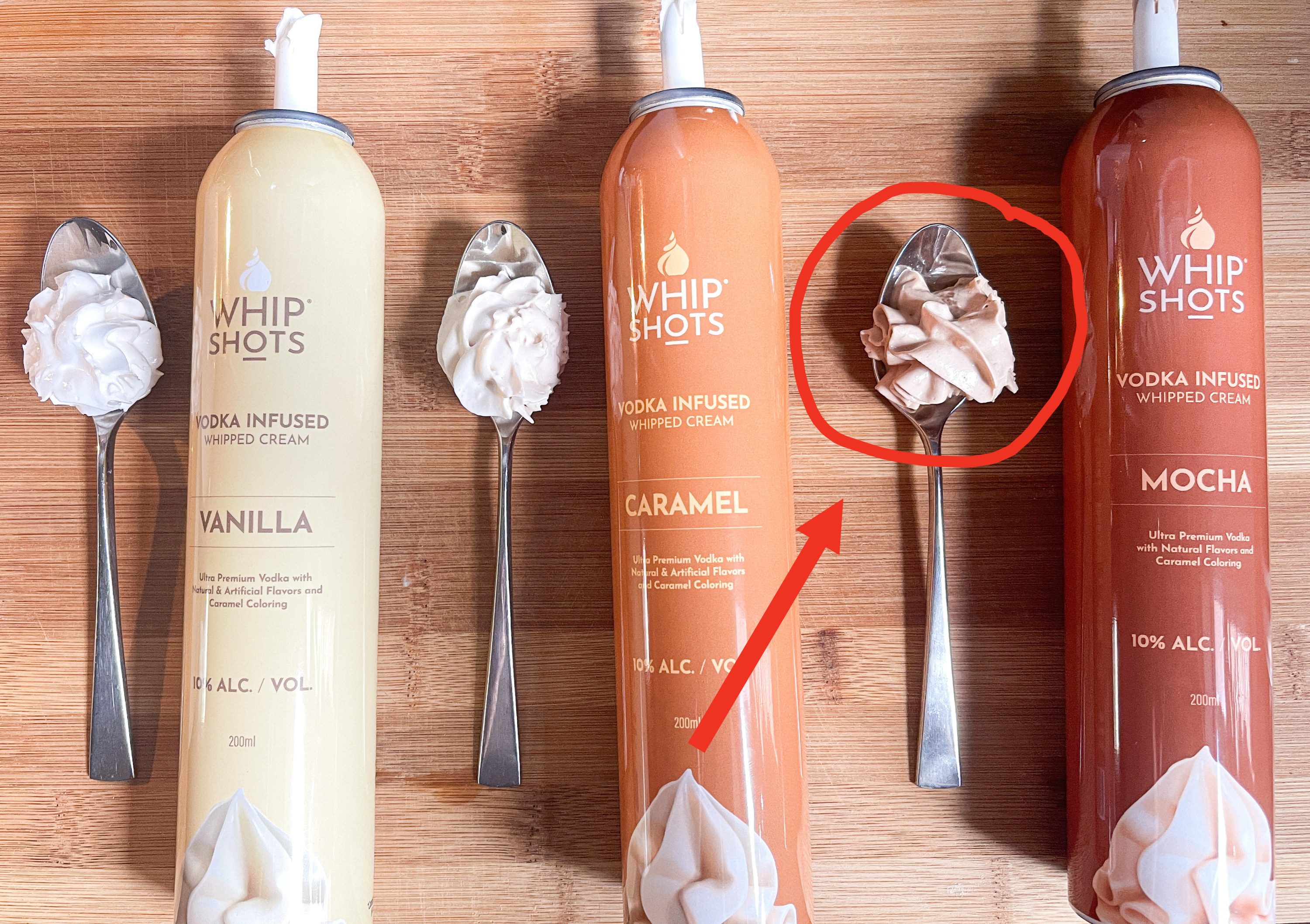 Three flavors of Whipshots (Vanilla, Caramel, and Mocha) with the whipped cream itself on three separate spoons; arrow pointing to the mocha whipped cream as the winner