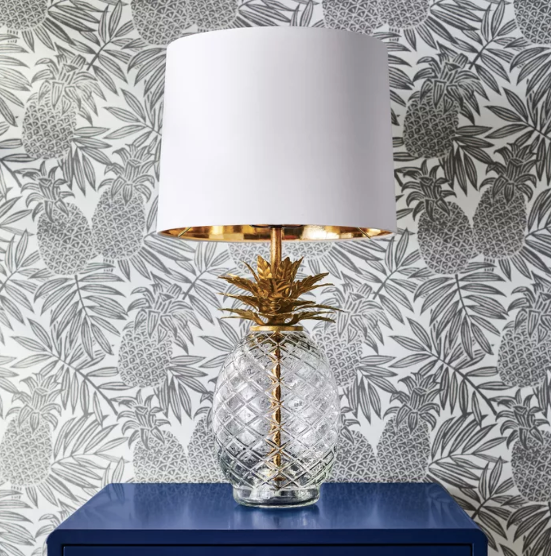 Brown and white pineapple wallpaper behind pineapple lamp and blue table