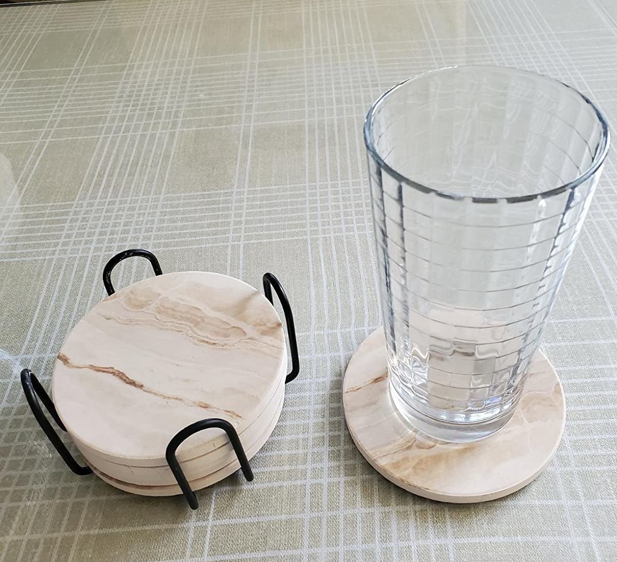 a reviewer shows five coasters stacked in its metal stand, with one sitting out with a glass on top