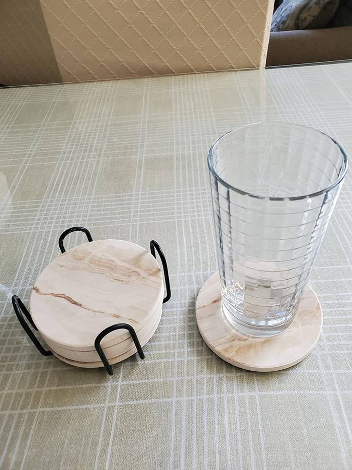 a reviewer shows five coasters stacked in its metal stand, with one sitting out with a glass on top