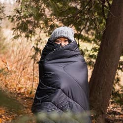 Model wrapped in the black blanket while standing in the woods