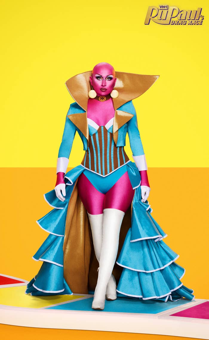 Maddy in a promotional photo wearing a striped and ruffled open dress with a bodysuit and a painted bald head