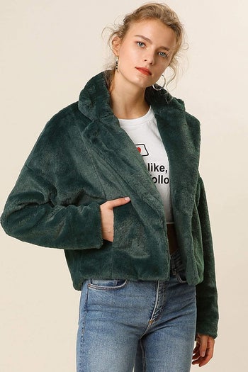 A model wearing the cropped open jacket in dark green. It hits at the waist