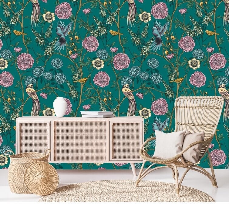 Emerald green wallpaper with yellow birds and flowers behind wicker chair and cabinet