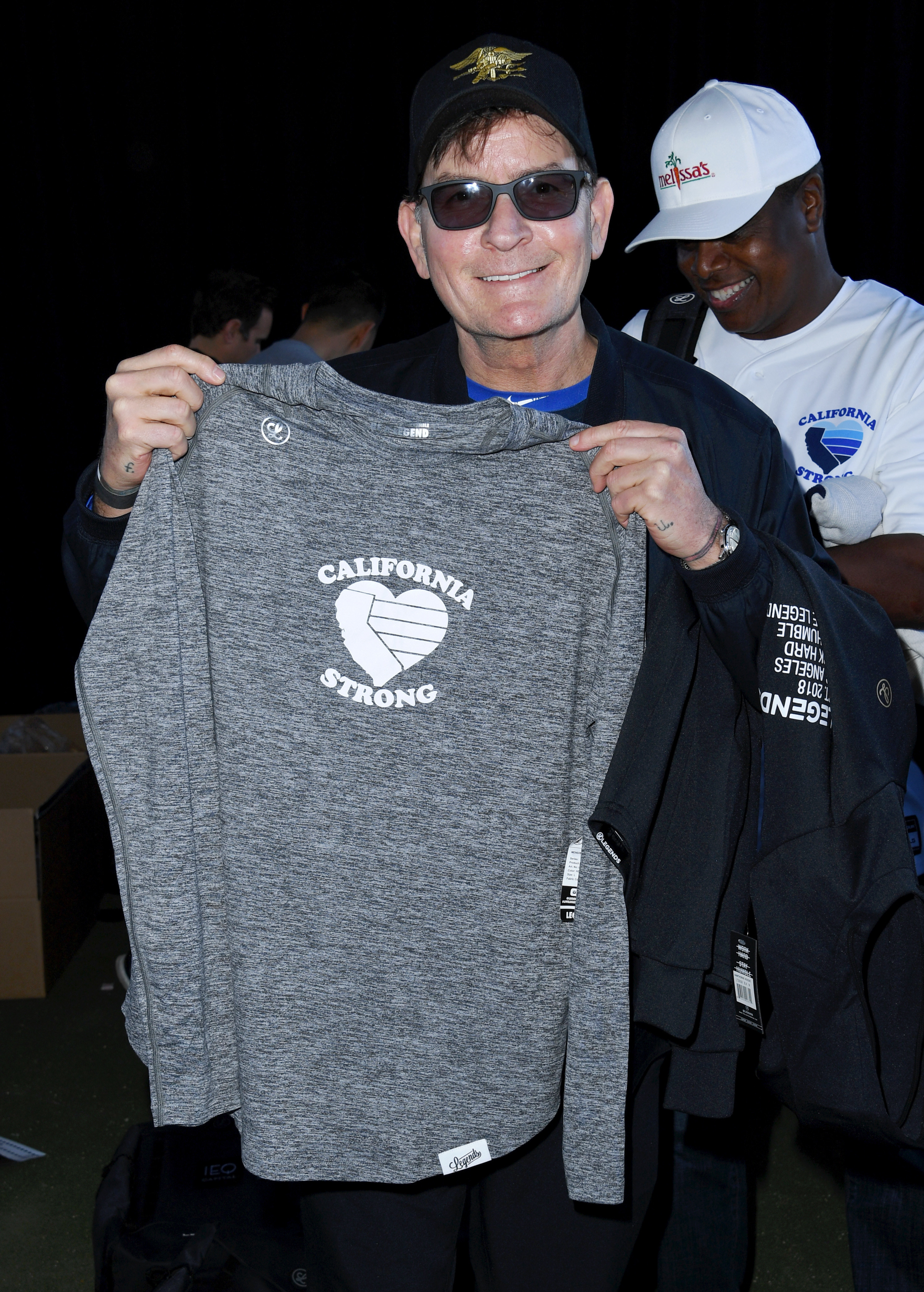 Charlie Sheen holding up a California Strong shirt and smiling