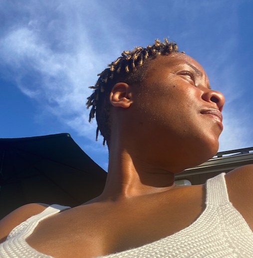 A young woman is looking away from the computer against a blue sky.