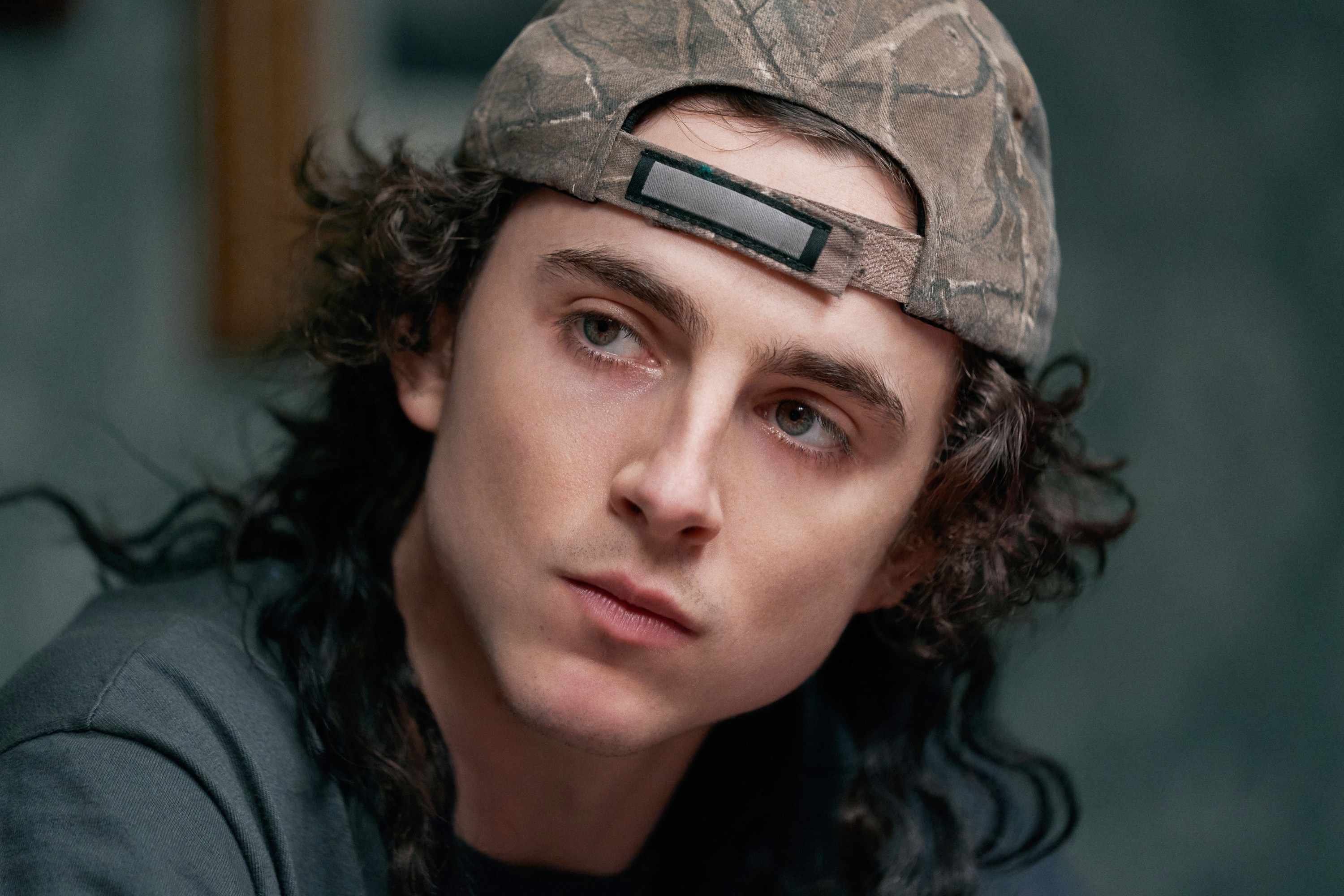 A close up of Timothée with a mullet and a backwards hat