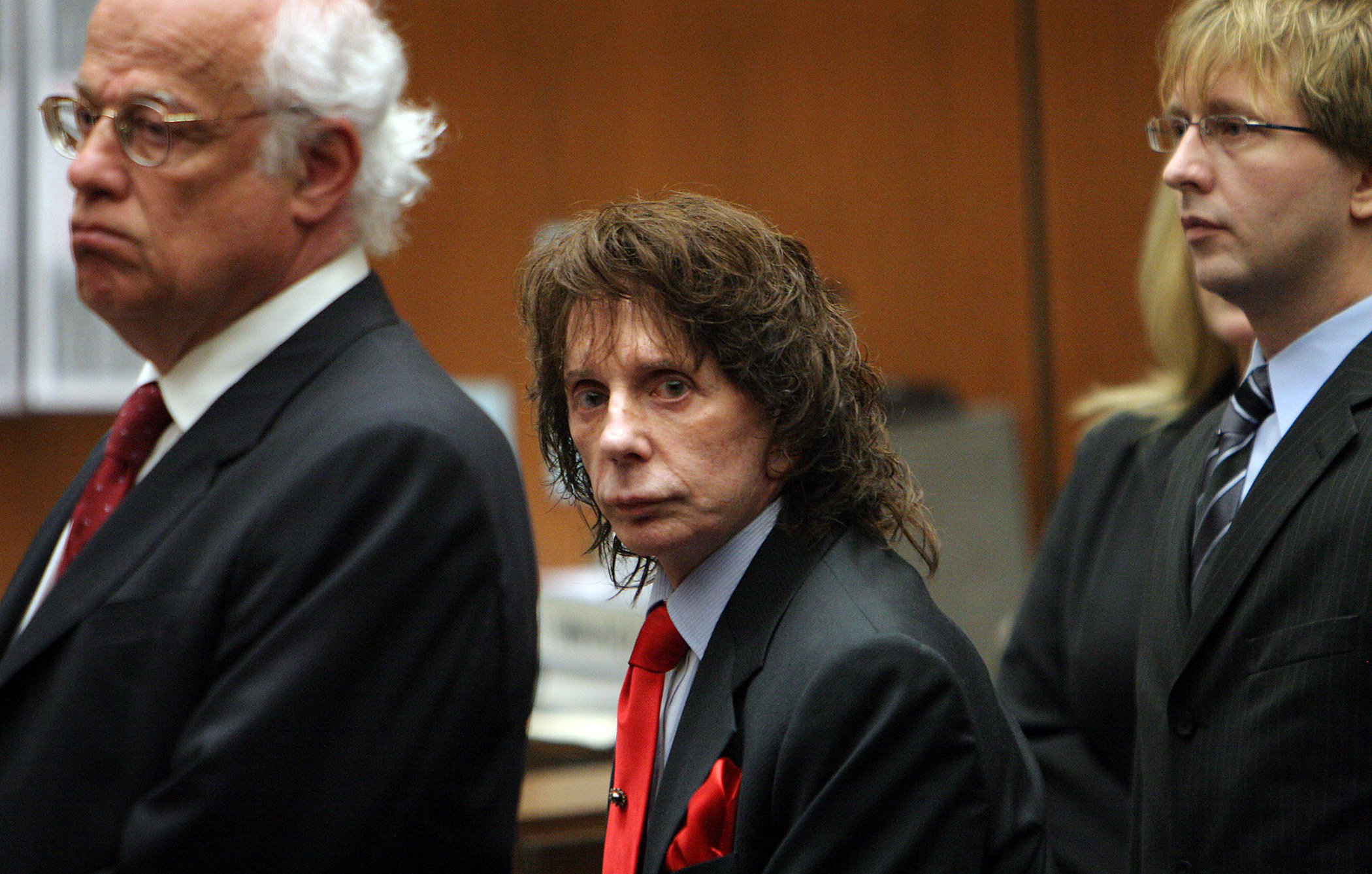 Phil Spector in between two lawyers in court looks at the camera