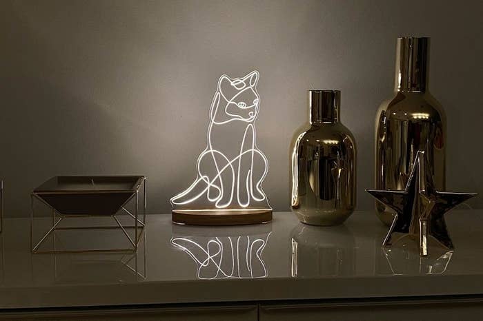 The white neon cat lamp on a desk next to a candle and other decorative accessories
