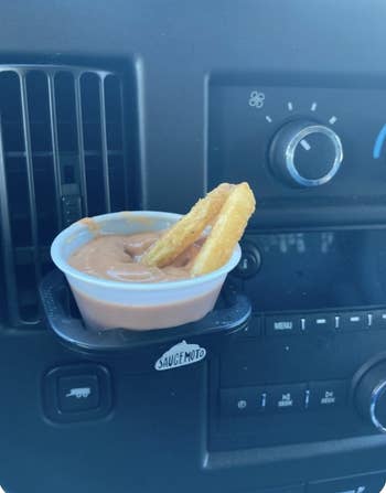reviewer showing two french fries in a container of dipping sauce attached to the car vent