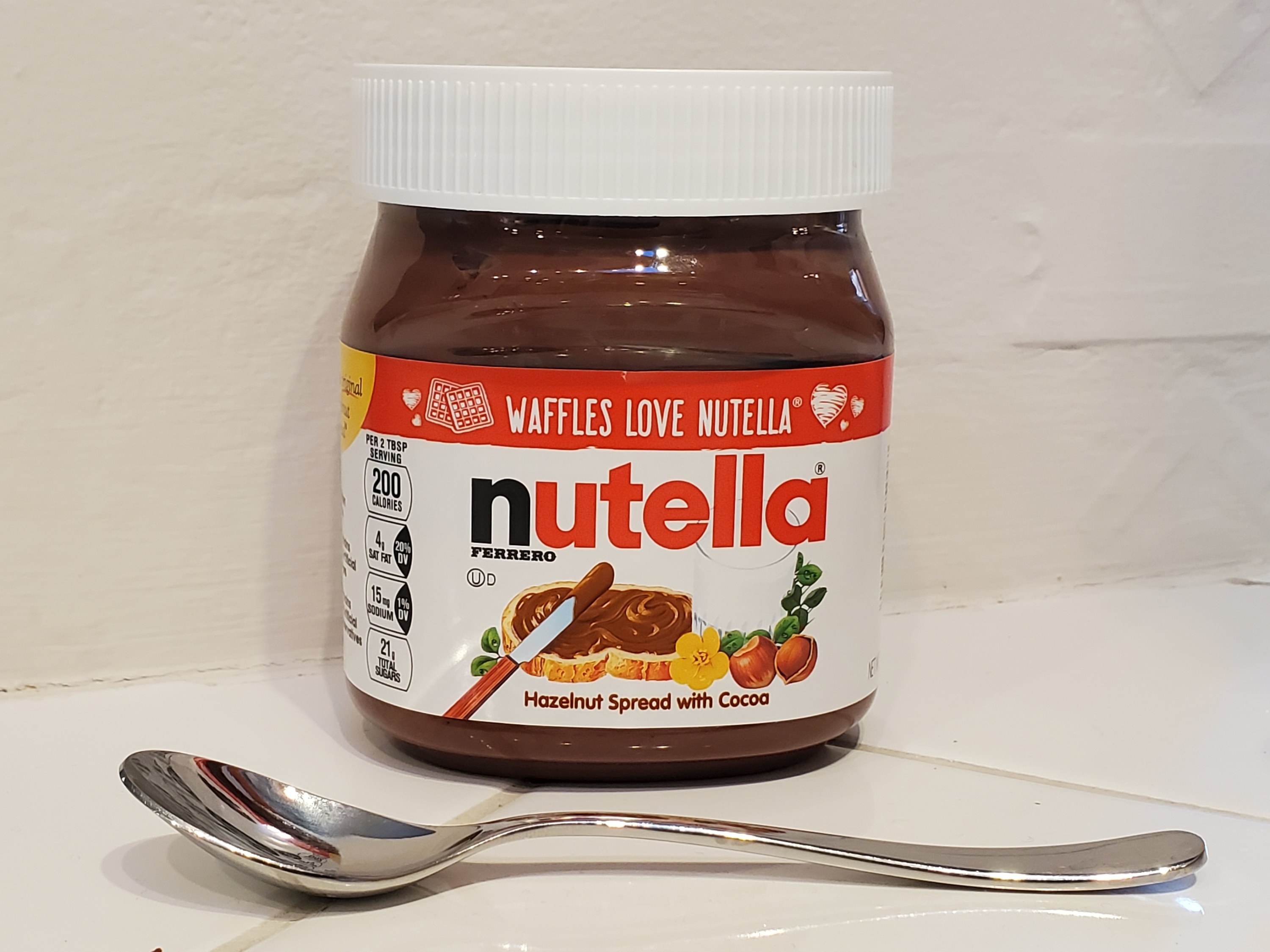 A jar of Nutella sitting on a countertop with a silver spoon next to it