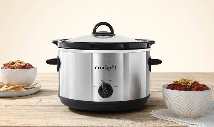 A silver crockpot on a light wooden table with chili around it