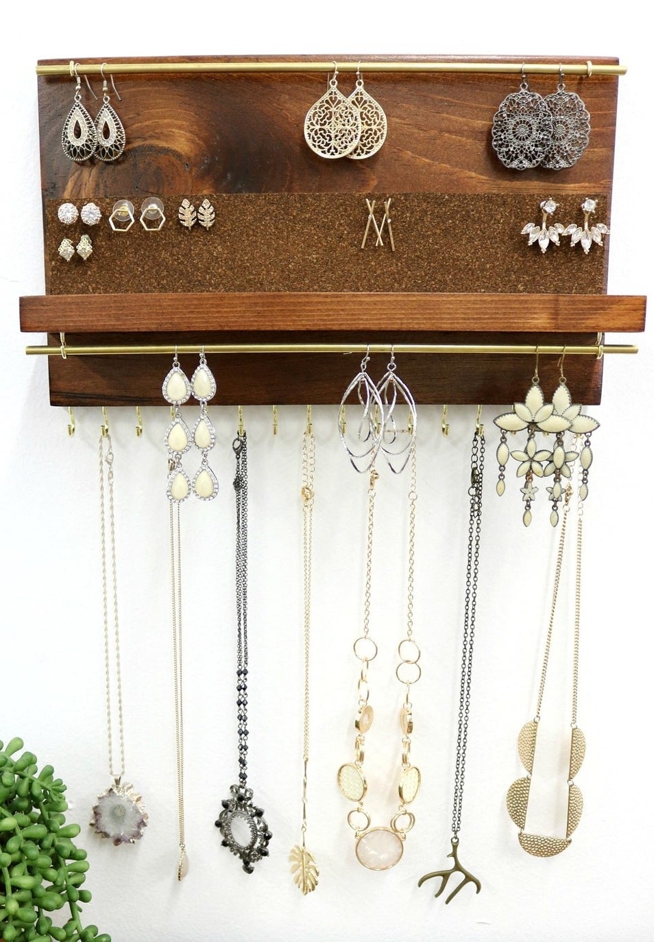 A wooden organizer with gold bars and hooks for storing necklaces, earrings, and other jewelry