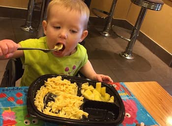 reviewer's photo of their child eating pasta on the disposable placemat stuck on a table