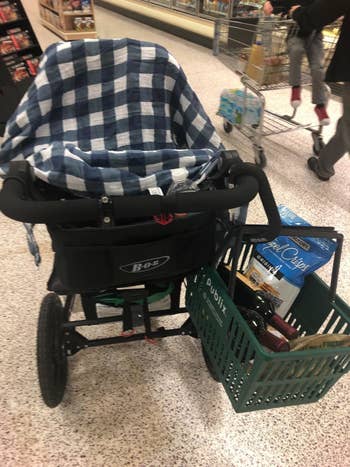 Reviewer's photo of the hook clipped onto their stroller holding a green grocery basket