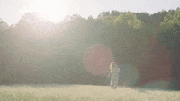 A woman gallivants in the sun on an open field.