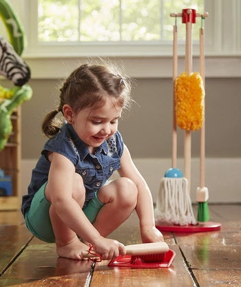 A child cleaning the floor with the duster and dustpan