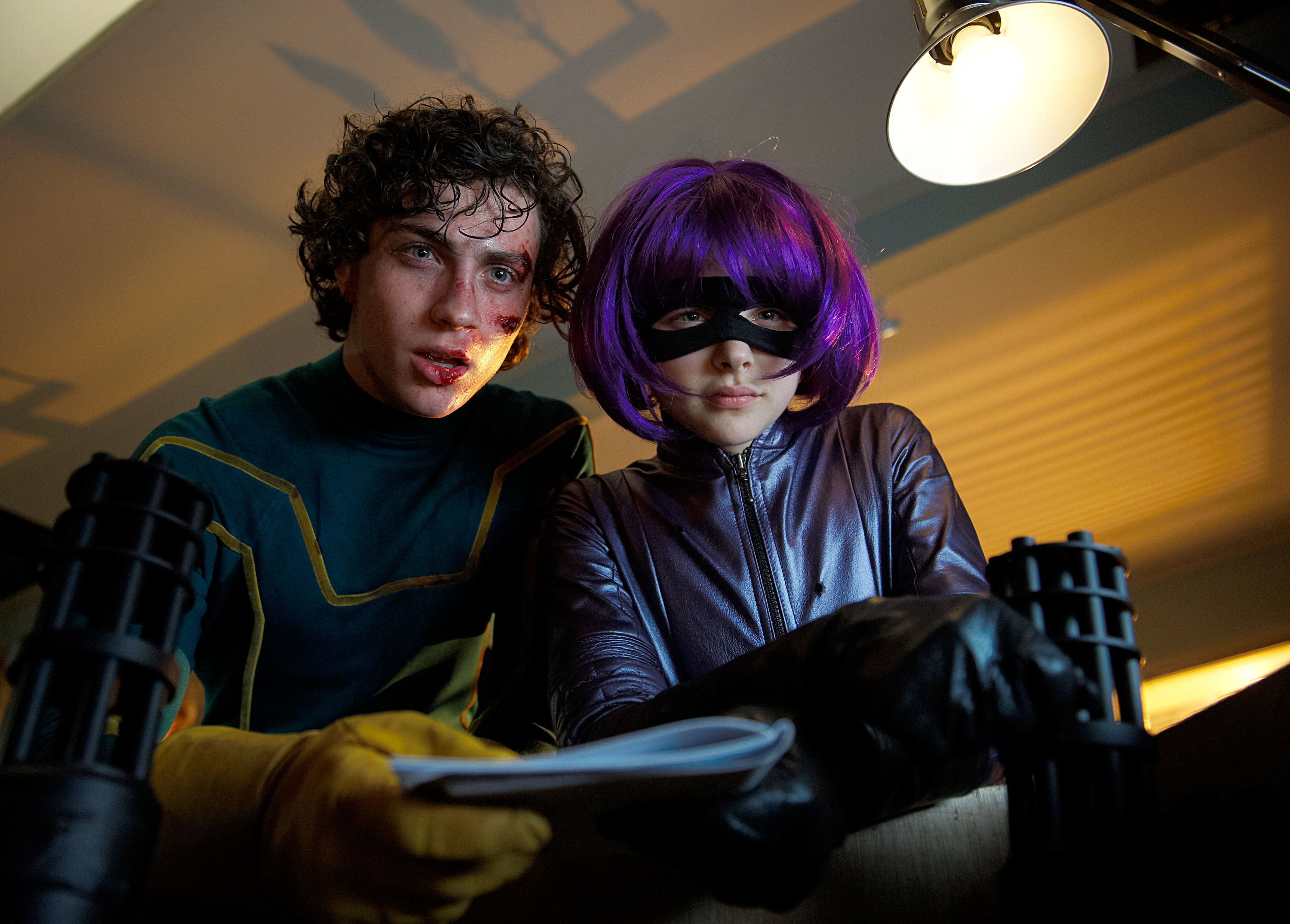 Aaron Johnson and Chloë Moretz wear superhero costumes and look down