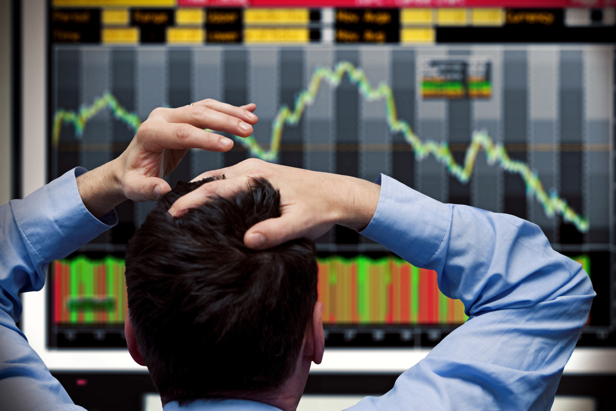 A man clutches his head in frustration while watching stock prices plummet