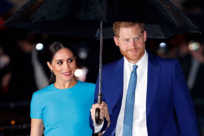 Harry and Meghan standing under an umbrella