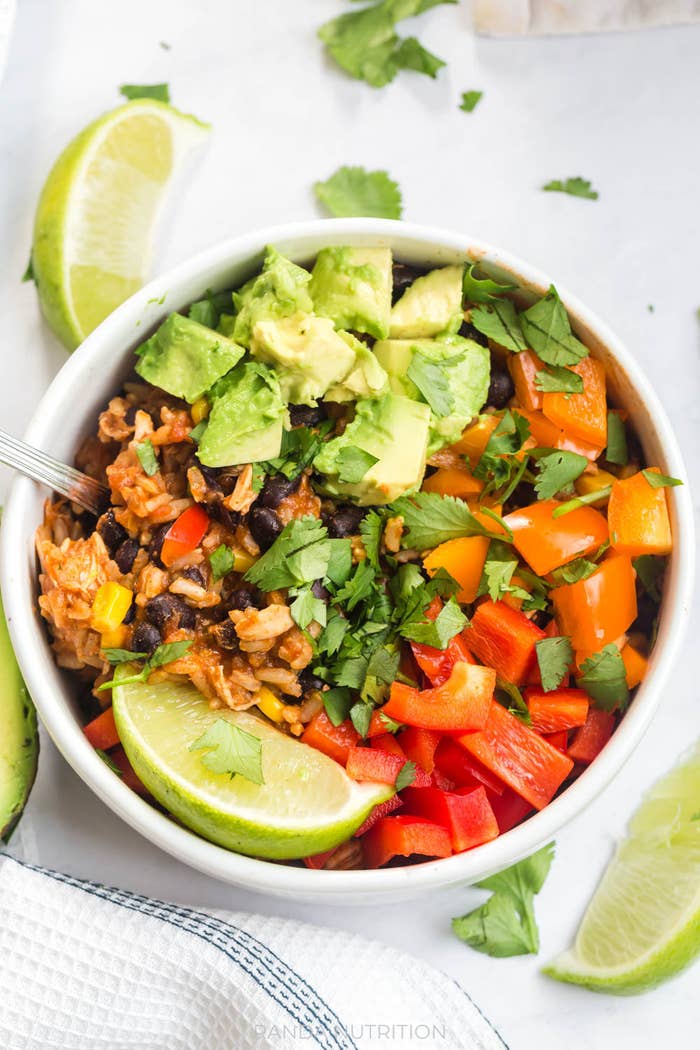 Chicken burrito bowl made of rice, beans, corn, red bell pepper, chicken, and topped with lime and avocado.