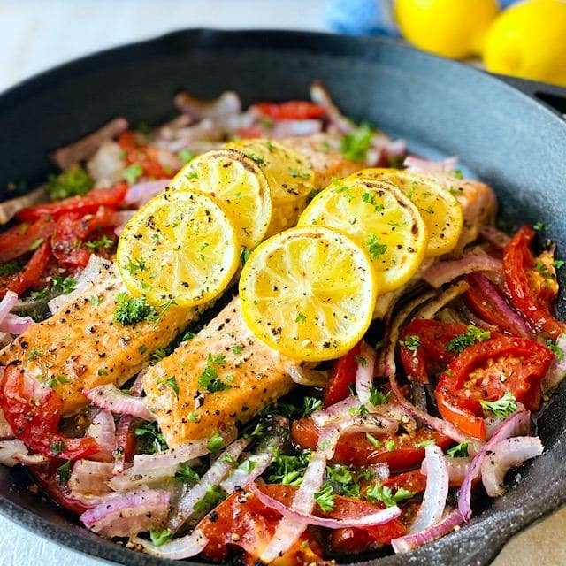 sliced of salmon on a cast iron skillet topped with lemon slices.