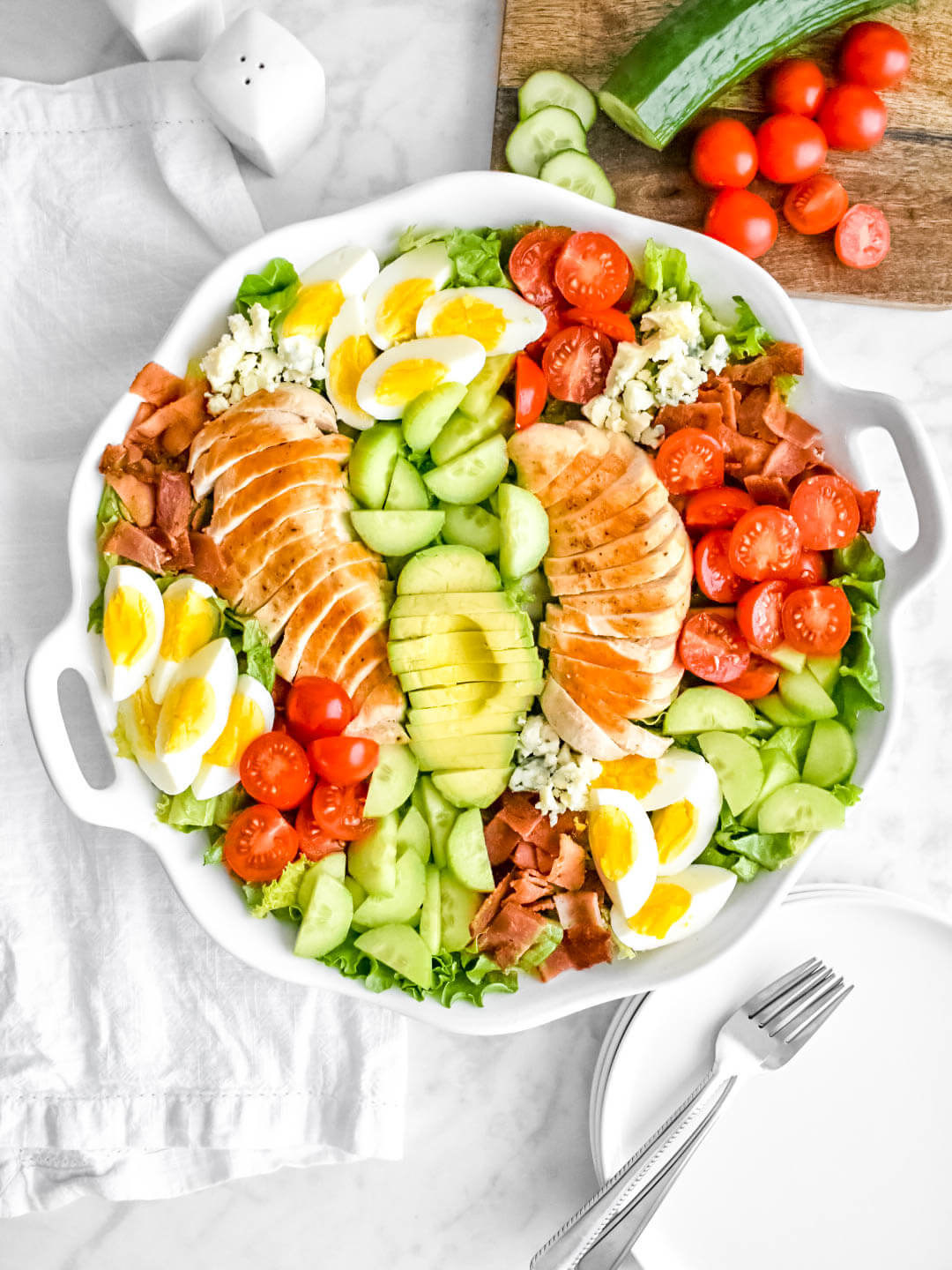 A bright and colorful cobb salad with cooked eggs, chicken, tomatoes, and cucumber.